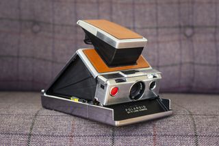 Polaroid SX70 camera angled front view and open in shooting position on purple chair
