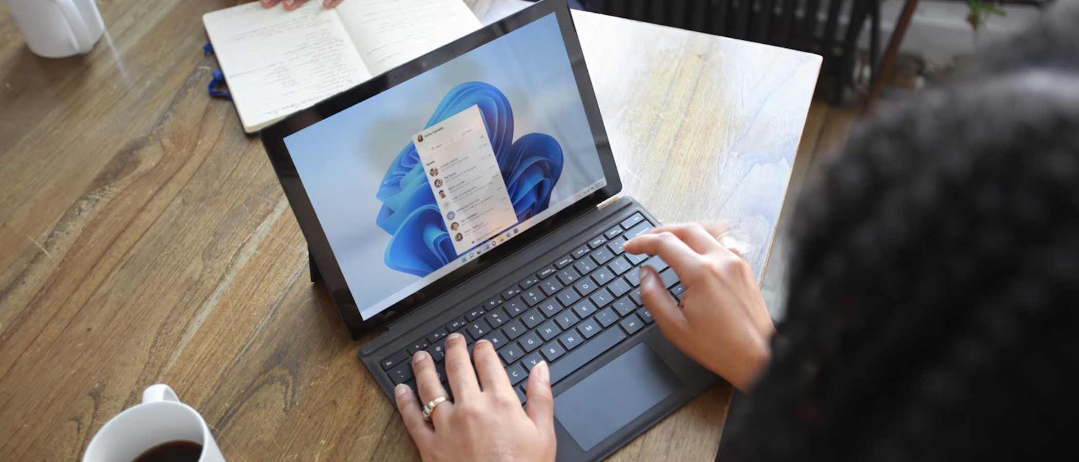 A woman at a table using a Windows laptop, opposite sits a man, neither show their face