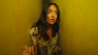 A disheveled Mary Kline looking scared while being stuck between two yellow walls in A24's Backrooms movie
