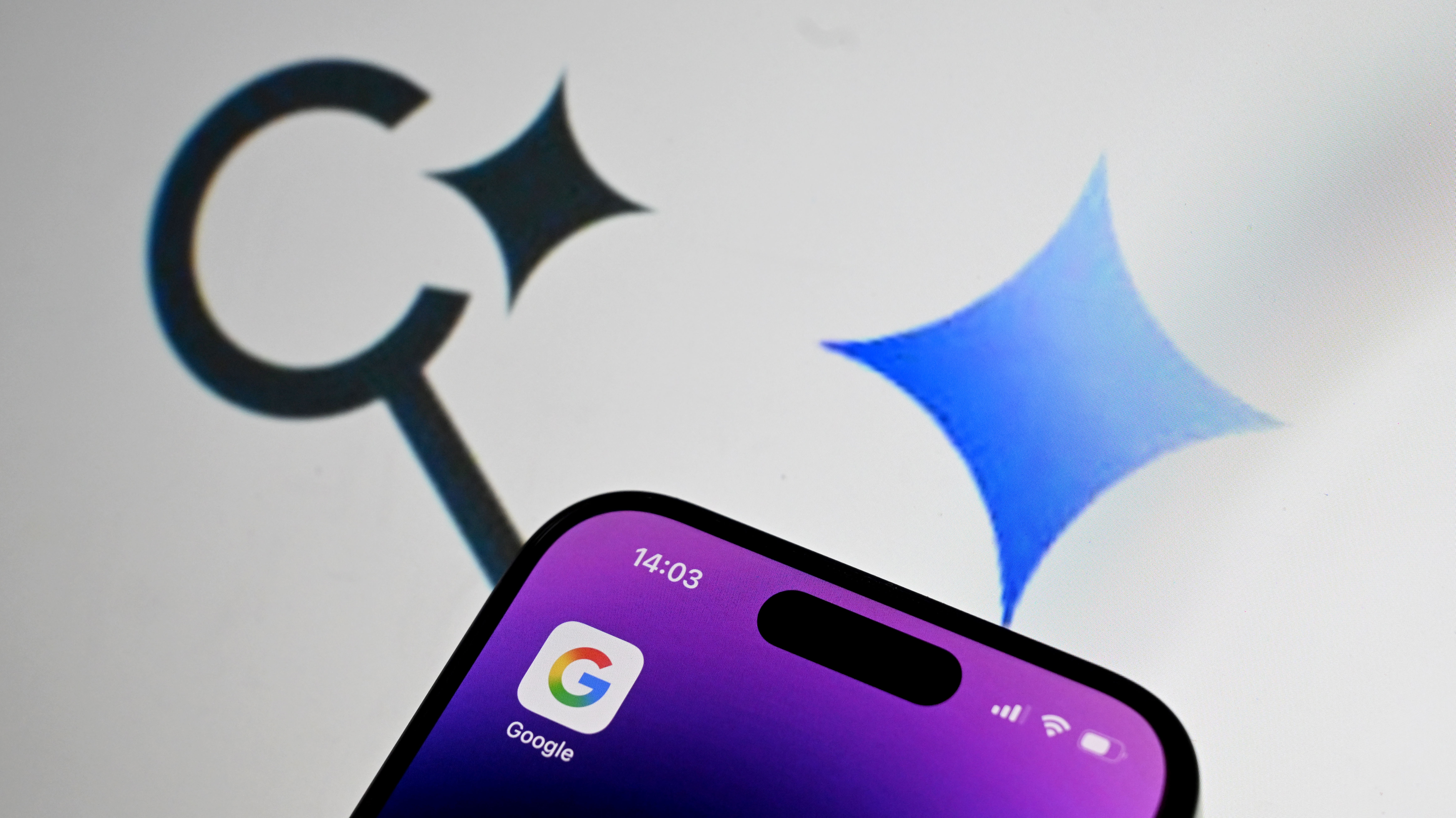 Google logo is being displayed on a mobile phone screen in front of a computer screen displaying AI Overviews and AI Mode logos.
