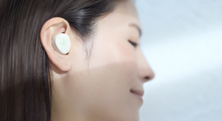 A woman in profile, wearing Audio-Technica's Mimio Assist One earbuds in white
