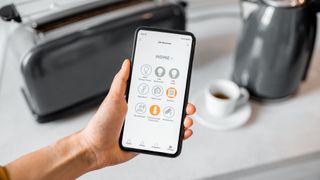 Someone holding a phone with an app controlling a smart kettle