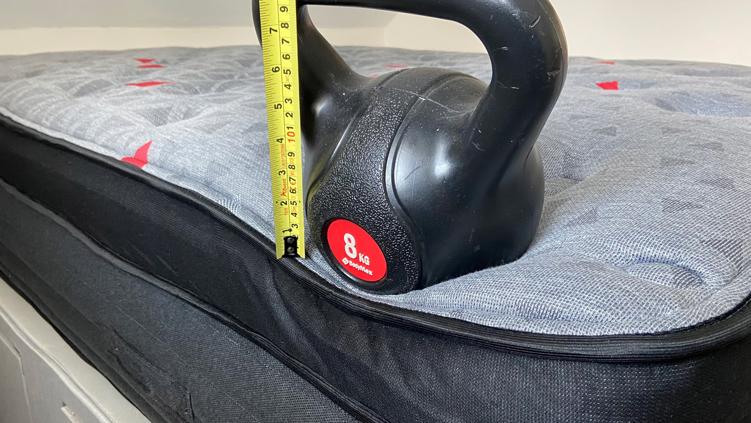 A weight on the edge of the Zoma Boost mattress. with a tape measure showing its sinkage