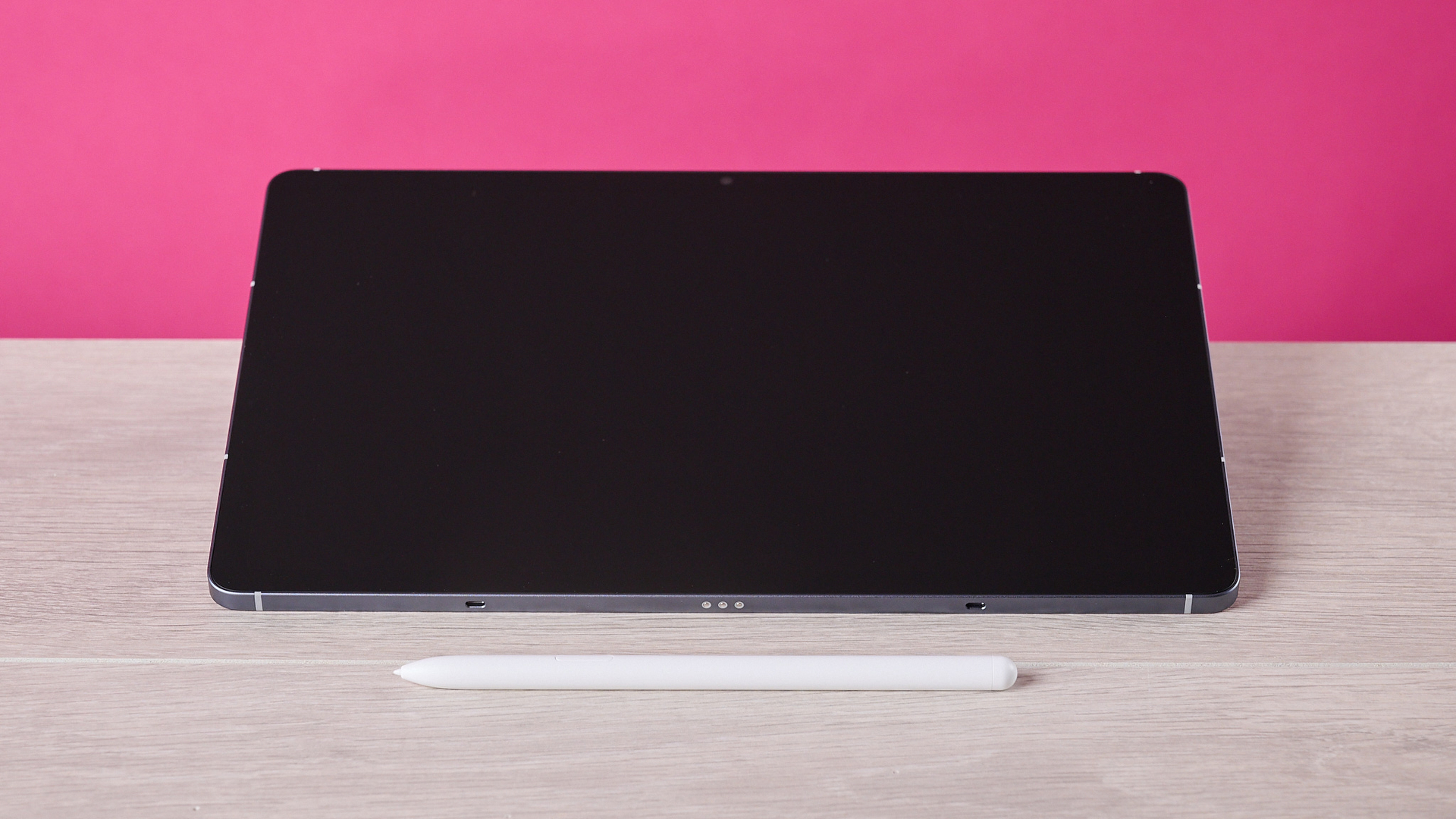 The Samsung Galaxy Tab S10 FE sat on a table behind the S Pen and in front of a pink background.