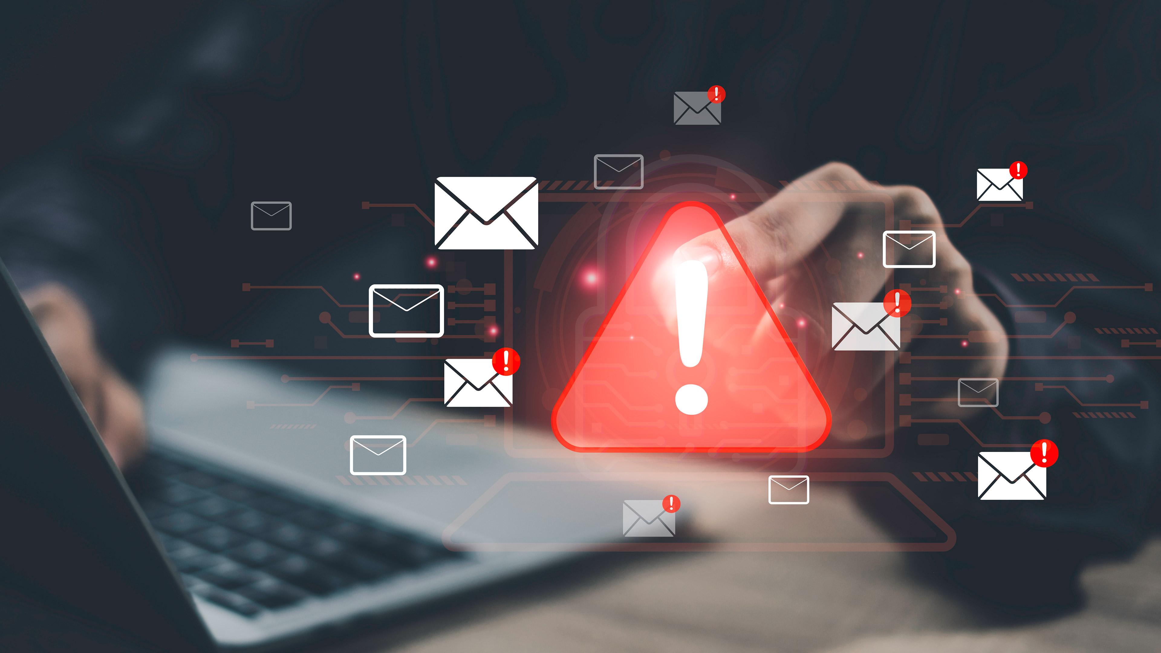 An exclamation mark inside a red warning triangle, surrounded by email symbols, superimposed on someone typing on a laptop