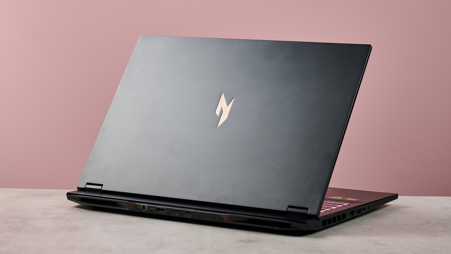 Three-quarter view of back of Acer Nitro 18 AI open on desk, with pink wall in background