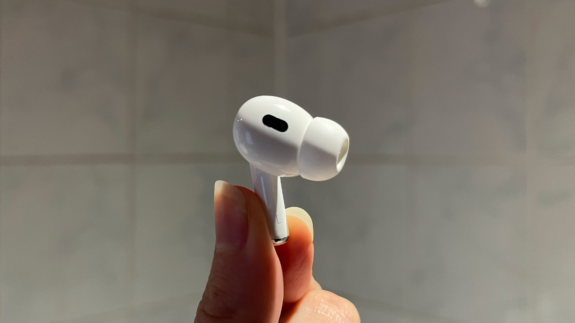 A hand holds a single AirPod